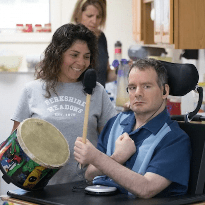 Man in wheelchair playing drum with support staff