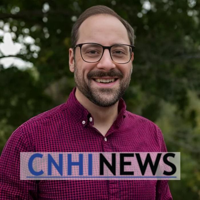 Man in glasses and red checkered shirt smiling outdoors.