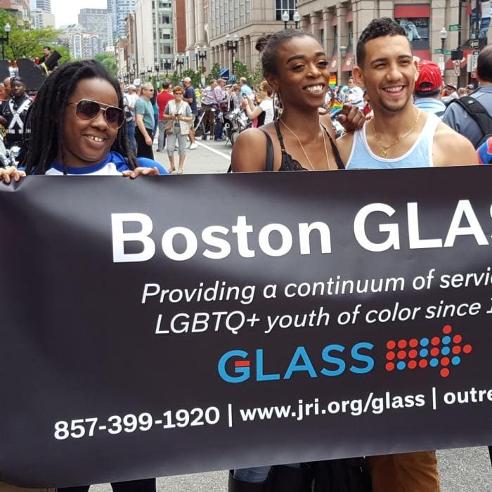 Three smiling people holding a Baltimore GLASS banner at a street event.
