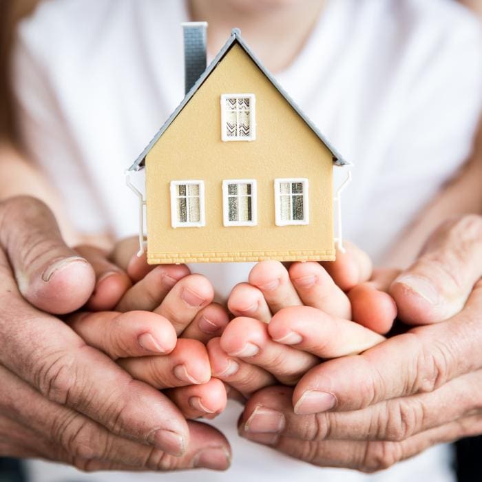 Multiple hands cradling a toy house.