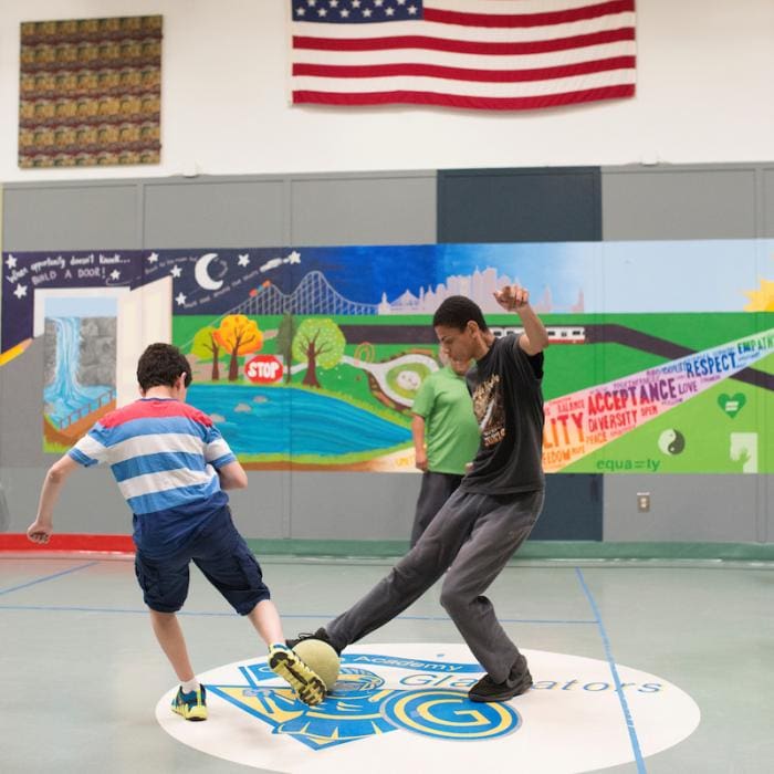 Two students playing soccer indoors.