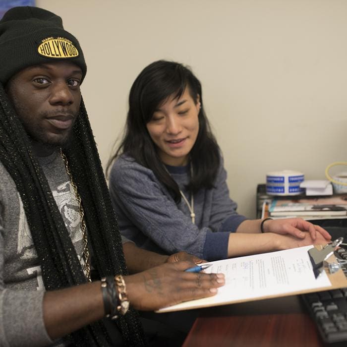 Two people sit at a table with papers, one holding a clipboard.