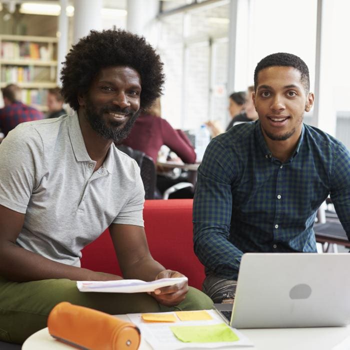 Two people sitting at a table with a laptop and papers, smiling at the camera.