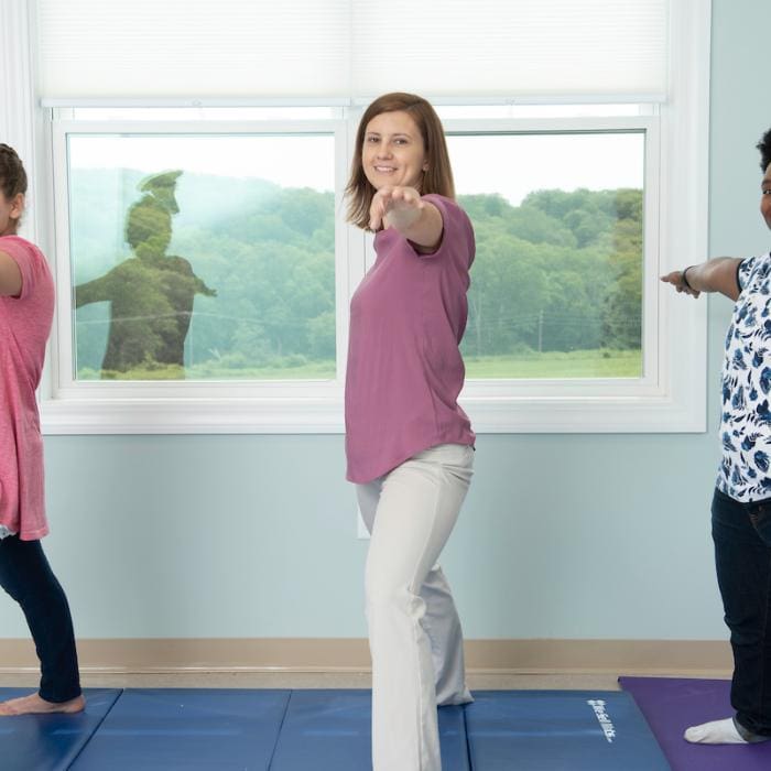 People on mats in yoga class, one person pointing at camera and smiling.