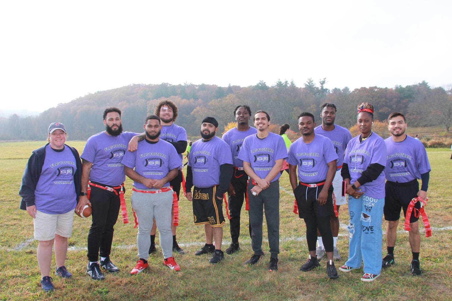 Group of people wearing purple T-shirts with a football logo, outdoors.