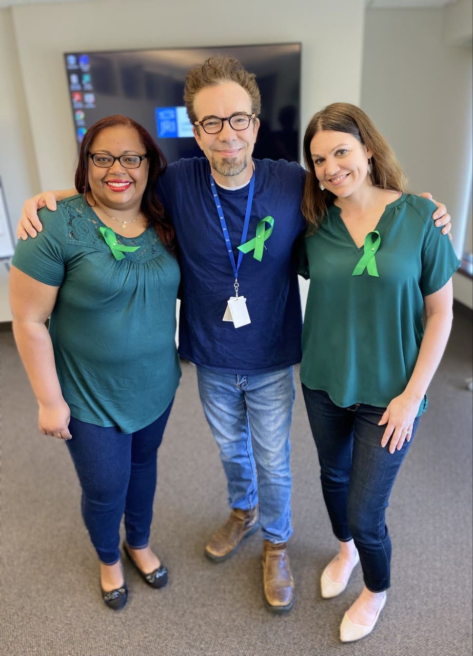 Mental Health Awareness Training Team with green ribbons on their shirts, smiling and hugging each other.