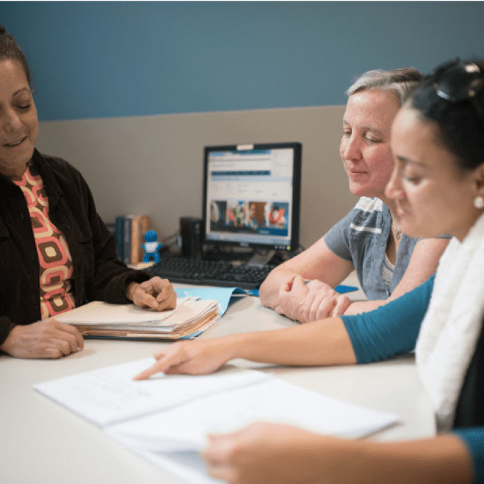Three people sitting at a table, looking at documents and a computer.