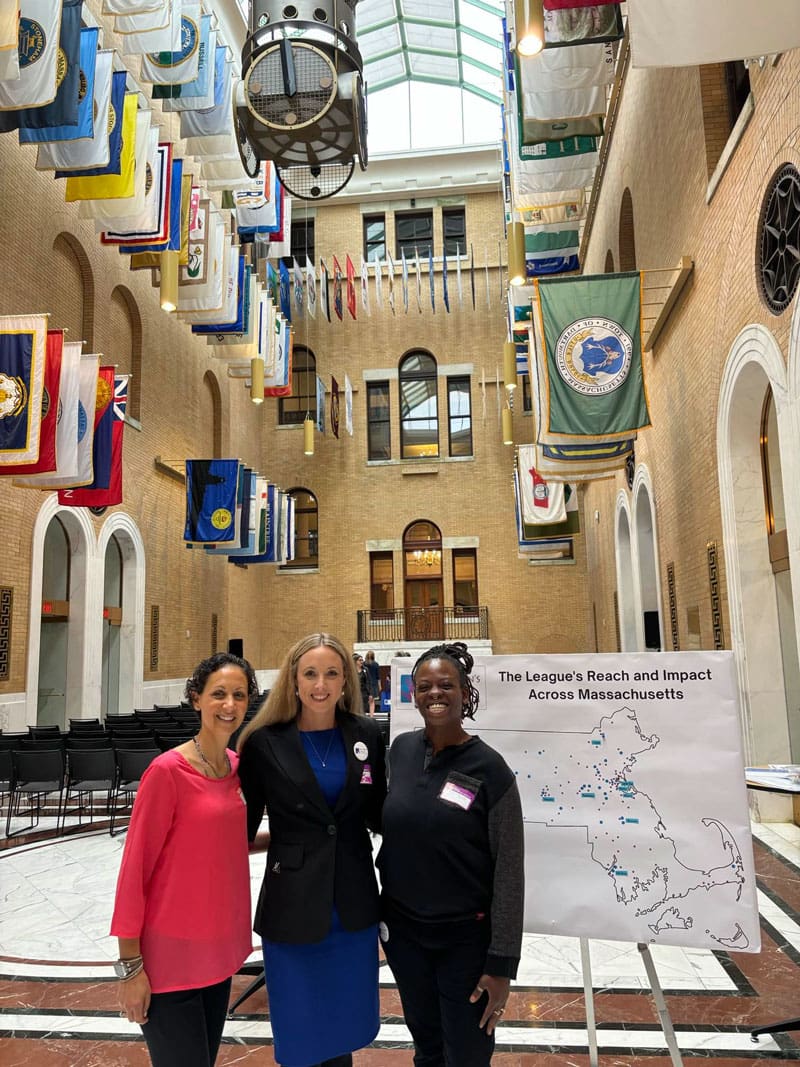 Three people standing in front of a map and banner, smiling, inside a building.
