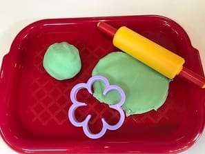 Play dough and flower-shaped cutter in a red tray.