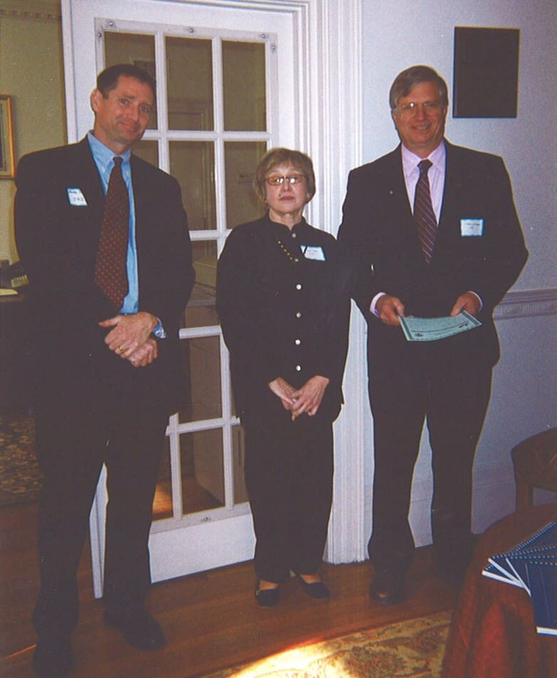 Three people in formal attire standing indoors, holding papers.