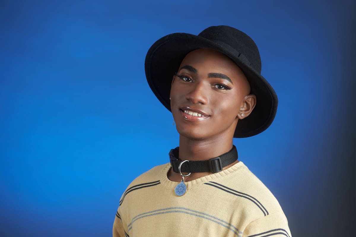 Person wearing a black hat, beige striped sweater, and a choker with a round pendant.