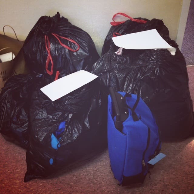 Four large black trash bags and a blue backpack on the floor.