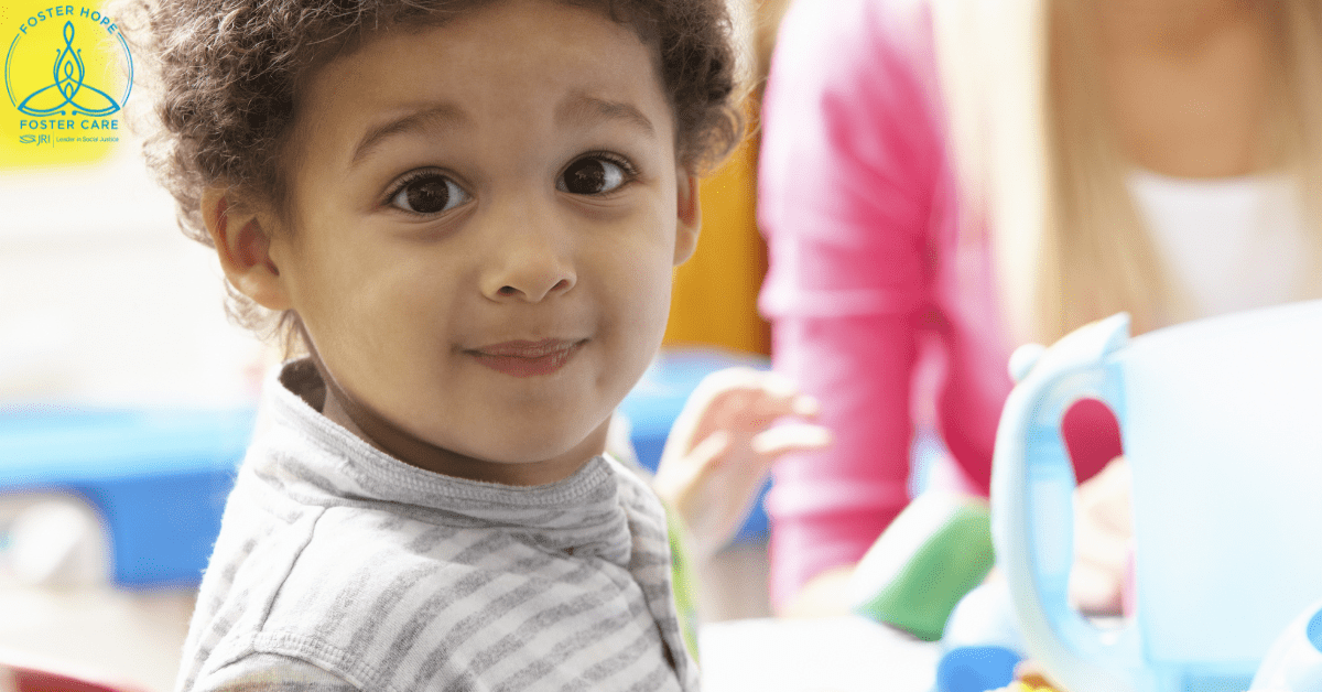 A child with curly hair and a striped shirt looks at the camera at a play table.