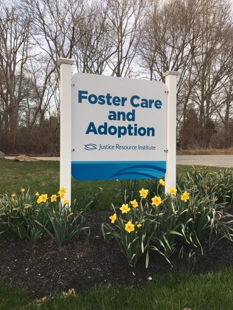 Sign reading 'Foster Care and Adoption' in front of flowers and trees.