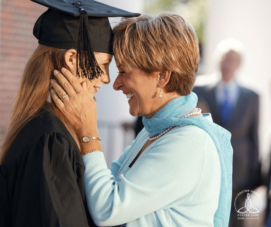 Woman in graduation cap and gown smiling at an older woman, who is smiling back.