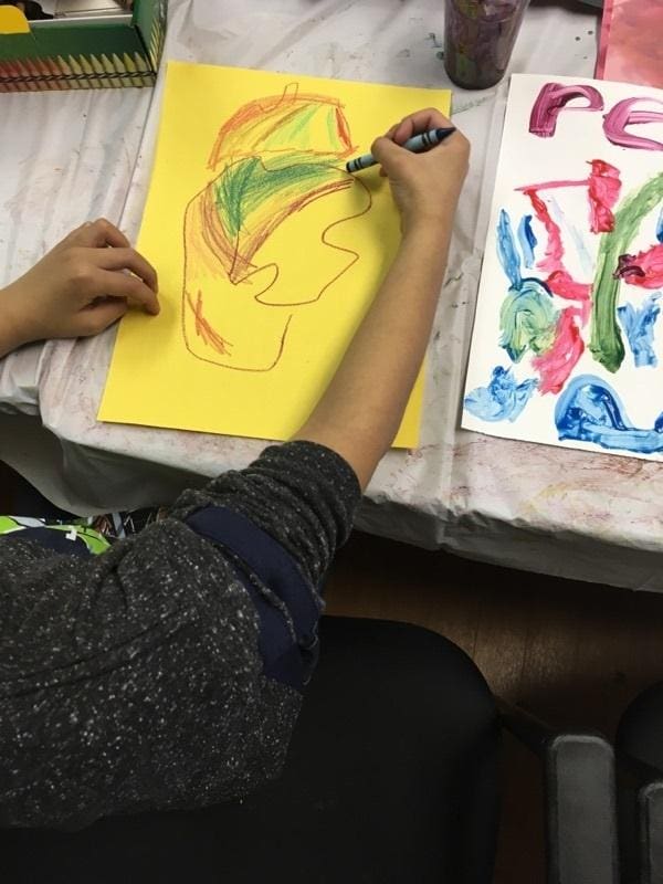 Person drawing a colorful abstract face on yellow paper.