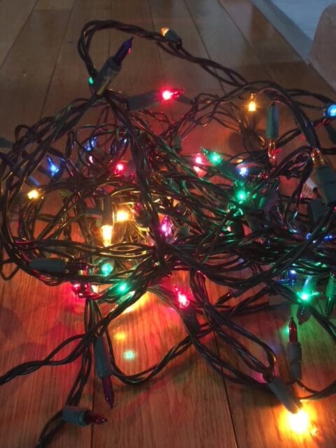 A tangled string of multicolored Christmas lights on a wooden floor.