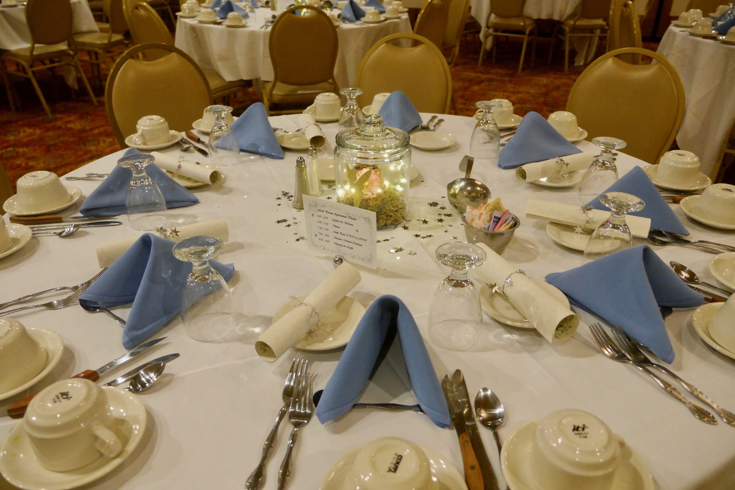 Round table set for a formal event with blue napkins and dinnerware.