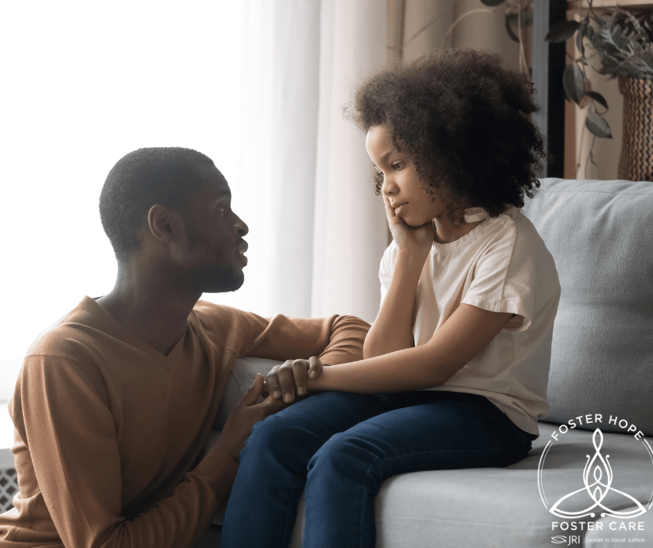 Young girl sitting on a sofa with her hand on her face, engaging with a man holding her hand.