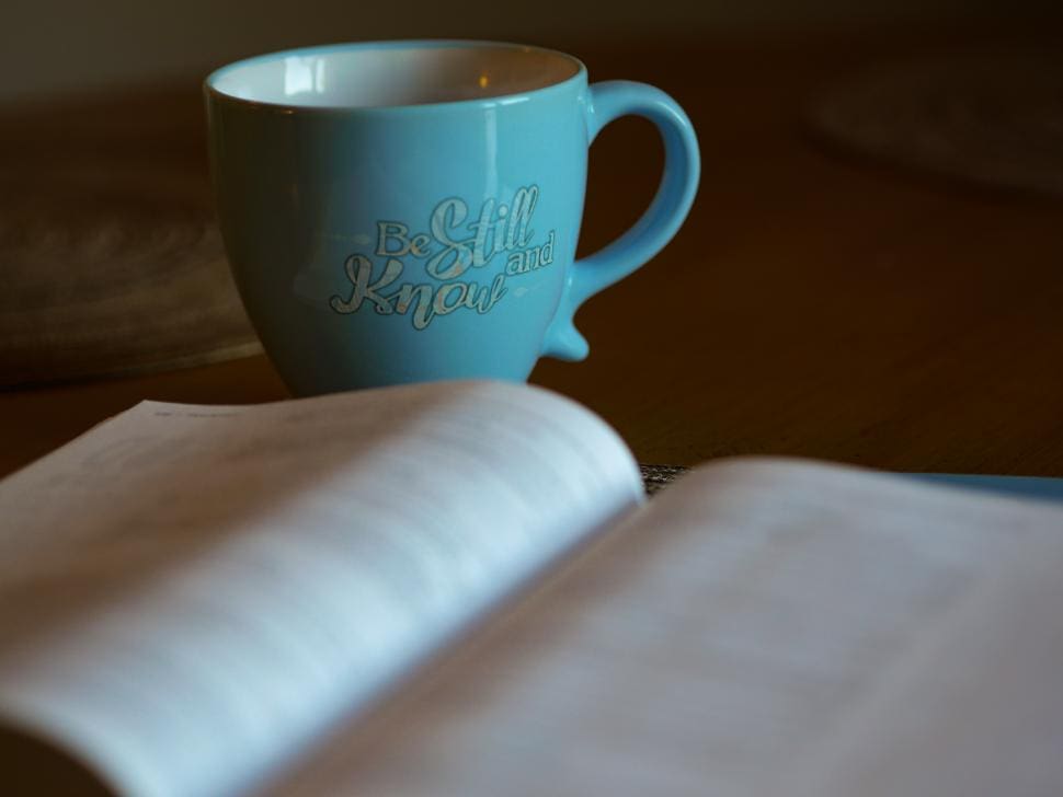 A blue mug with the words "Be Still and Know" on a table.