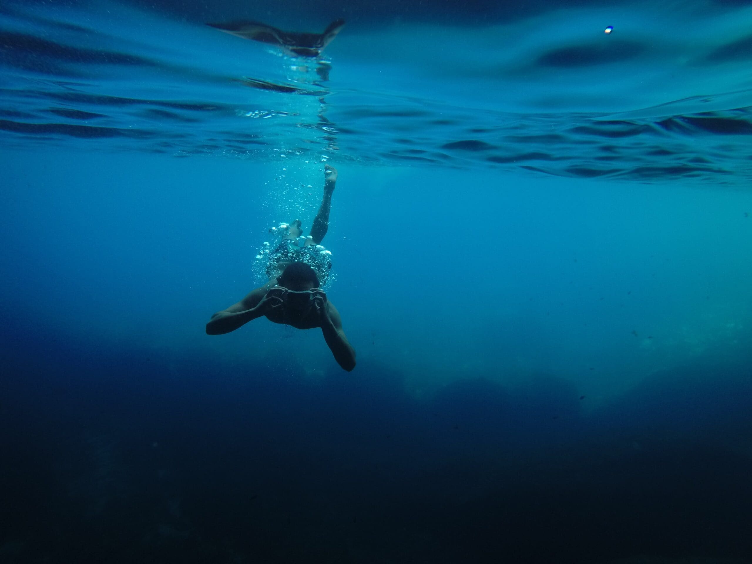 Person swimming underwater with goggles, front view.