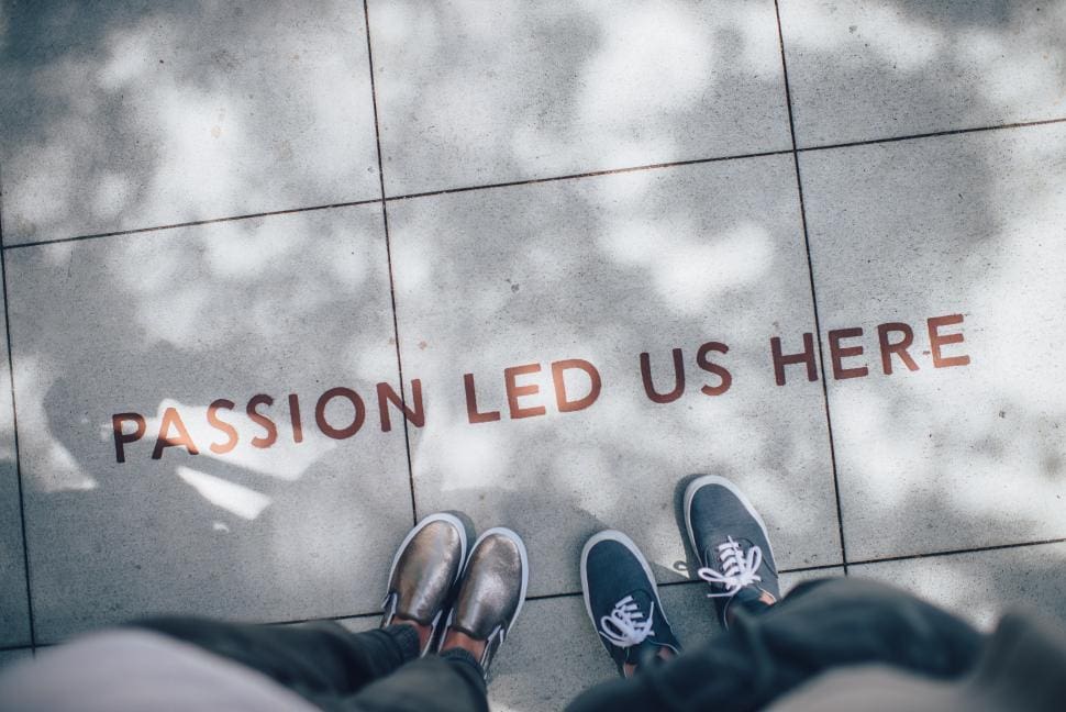Two people standing on a tiled floor with the words "PASSION LED US HERE"