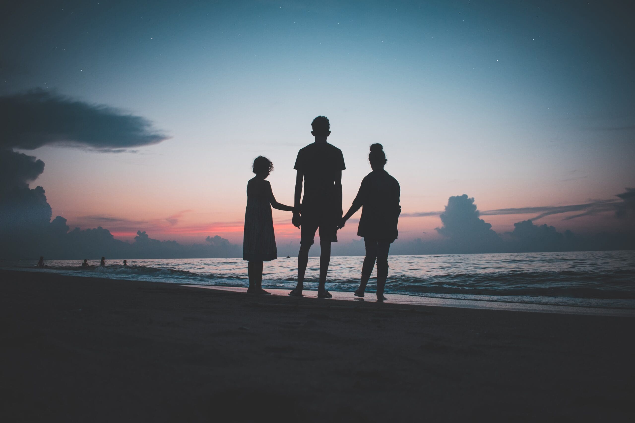 Silhouettes of adult and two children holding hands on the beach at sunset.