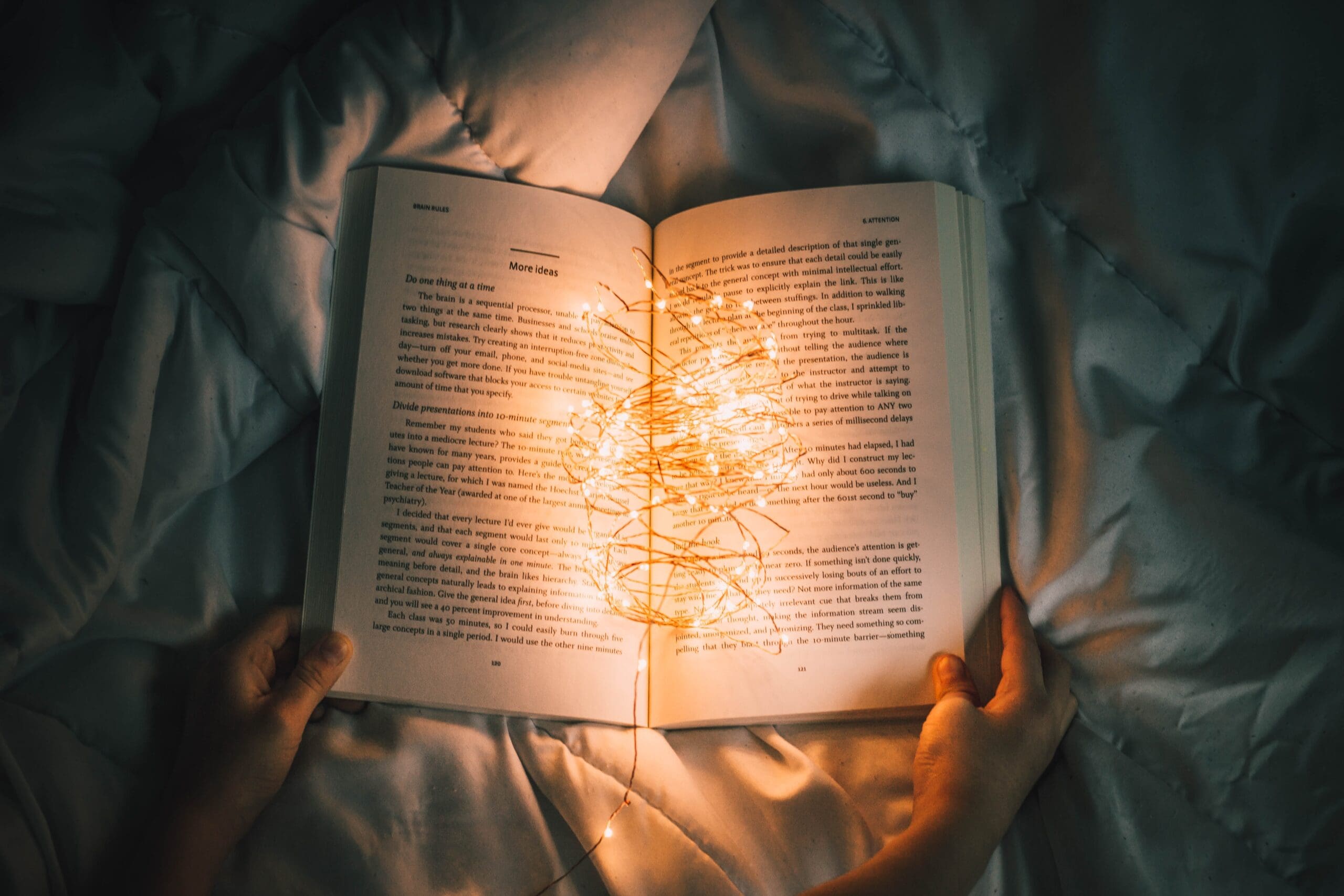 Open book with text and string lights on pages, held over a quilted surface.