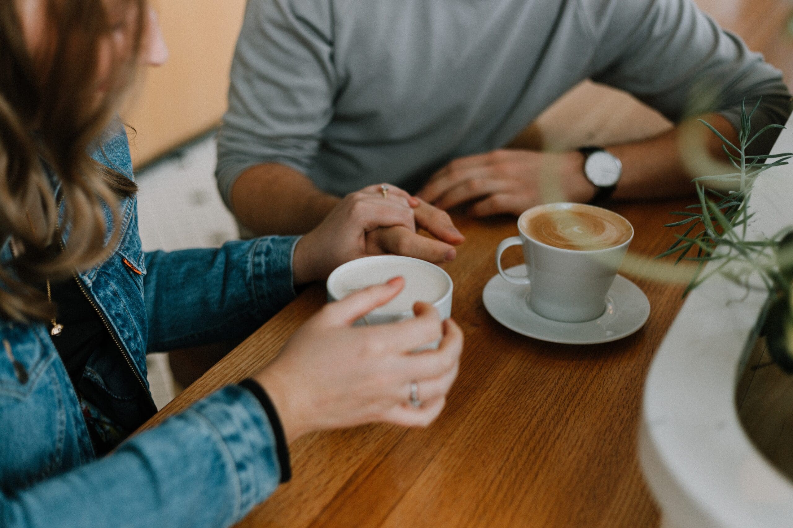 Two people holding hands across a table with coffee cups.