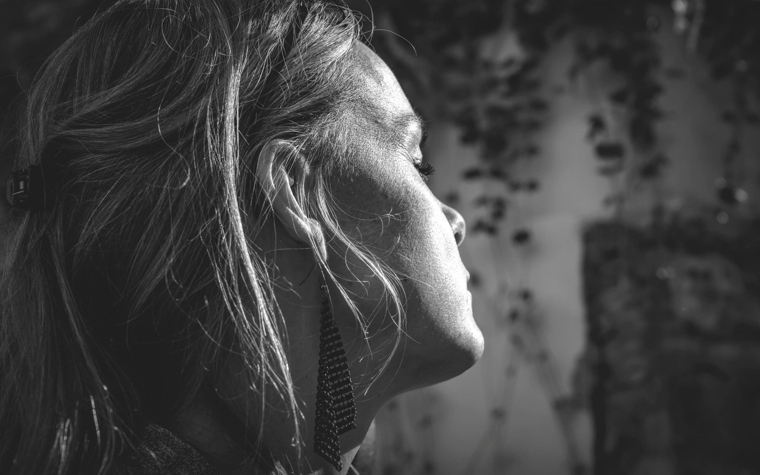 Close-up of a person with long hair and earrings, eyes closed, in black and white.