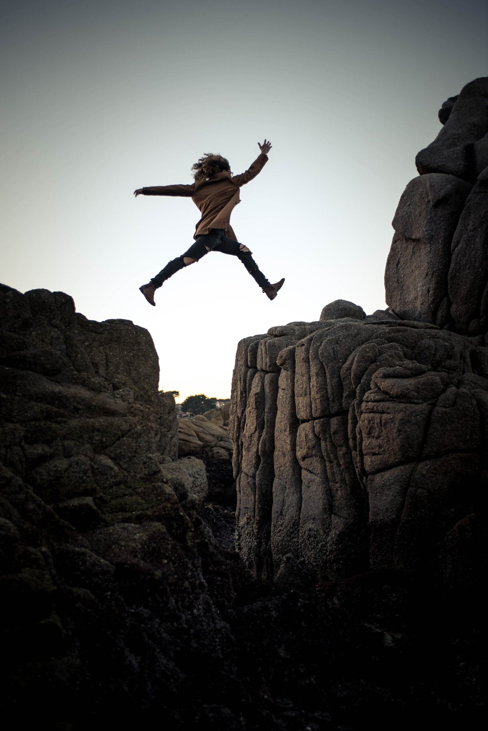 Person jumping between rocks at sunset with arms spread wide.