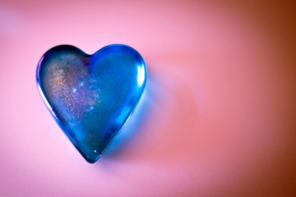 Blue heart-shaped glass object on pink background